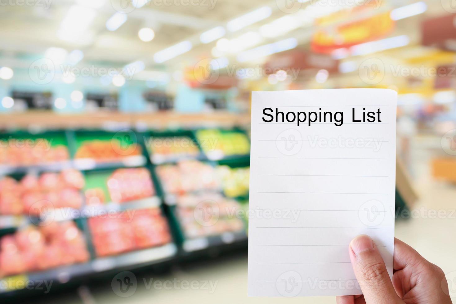 hand hold shopping list paper over supermarket blur background photo