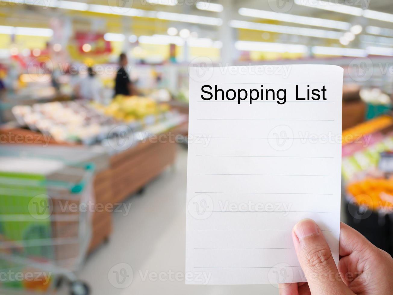 mano femenina sosteniendo papel de lista de compras en el fondo borroso de la tienda de comestibles foto