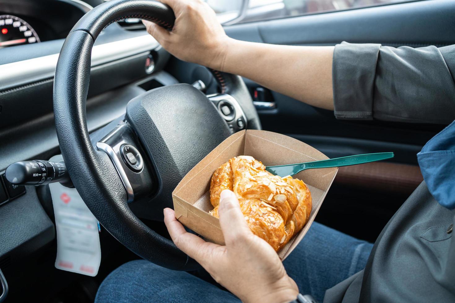 Asian lady holding ice coffee and bread bakery in car dangerous and risk an accident. photo