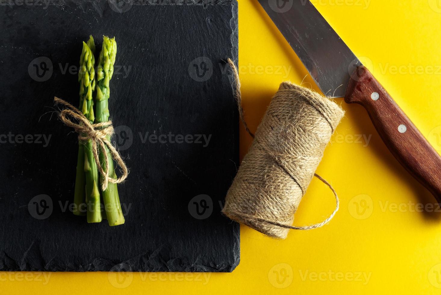 Asparagus. Bunch of fresh asparagus tied on a plate of slate with a knife and a roll of string on yellow background. Healthy vegetarian food. Horizontal image. photo