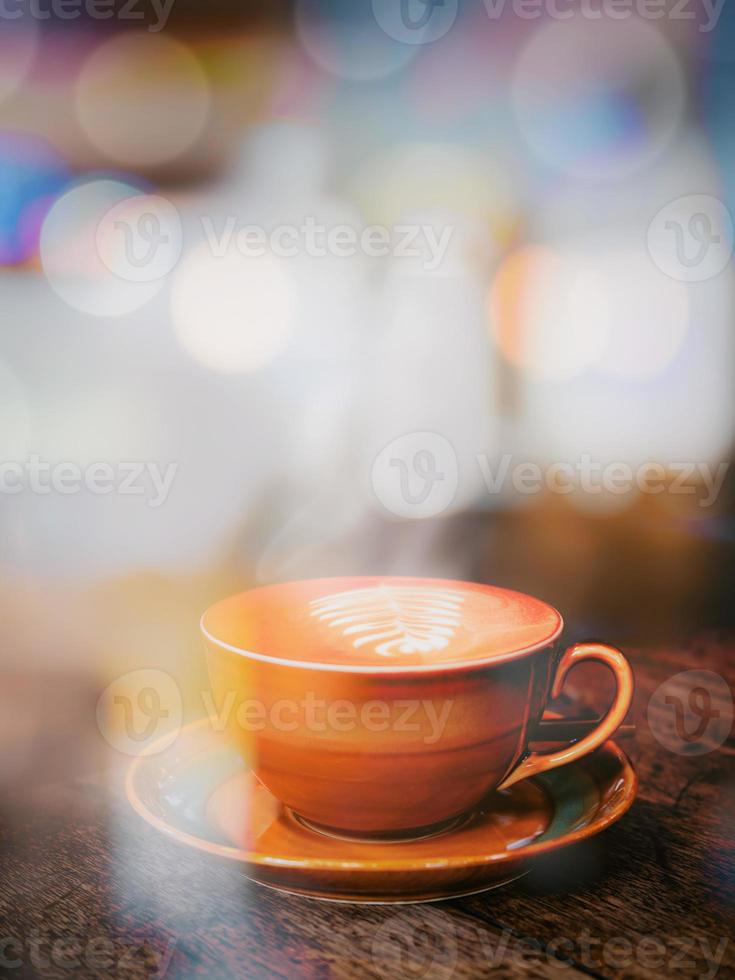 A view through the window glass of a hot coffee cup on an old wooden table in a cafe. photo