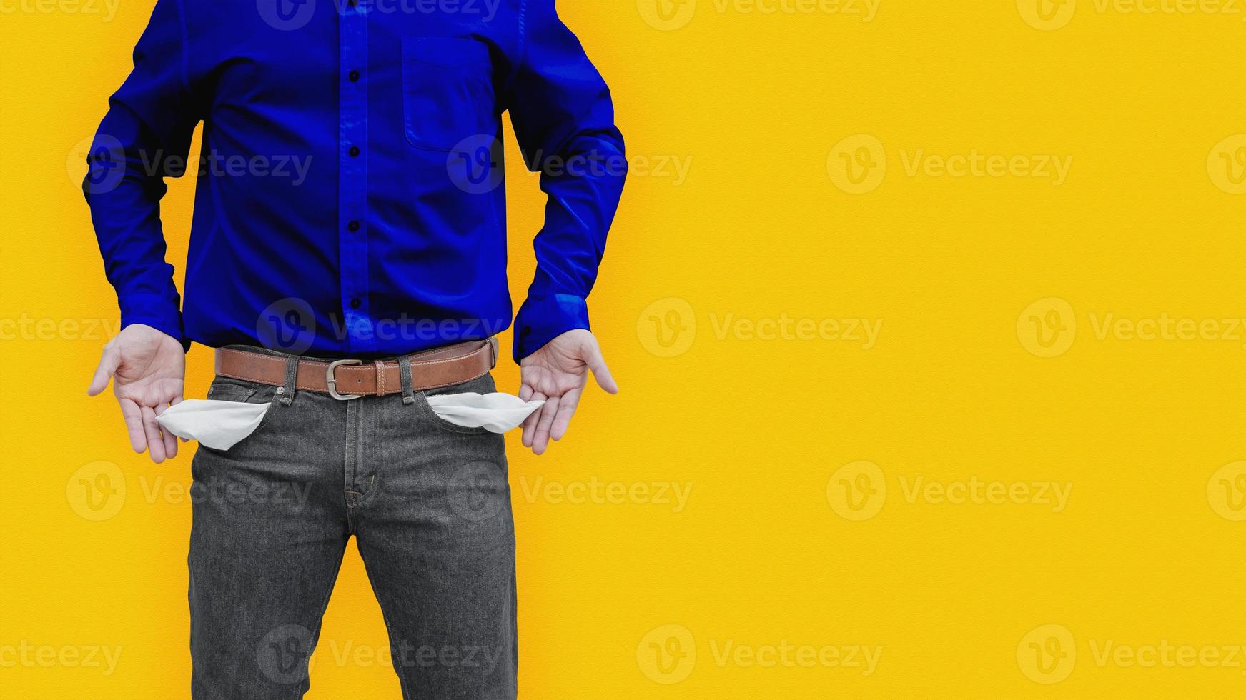 Man showing his empty pockets on yellow wall background. photo