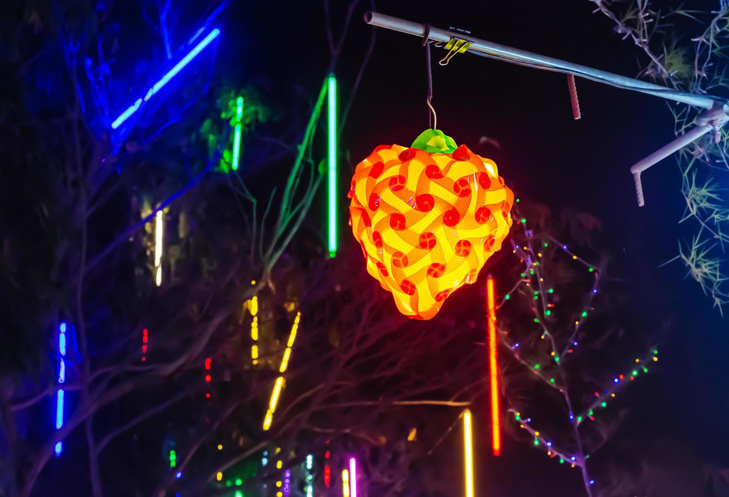 Strawberry shaped lamp hanging with blurred bokeh of colorful lights on the tree photo