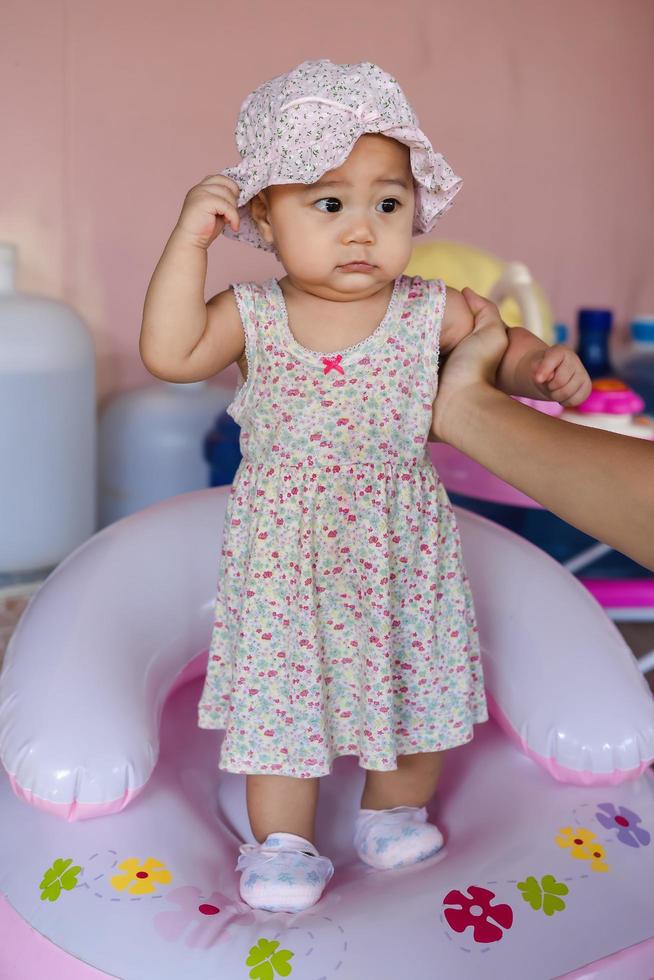 Portrait of a little Asian baby child girl supporting by her mother's hand and looking at or something or her mom photo