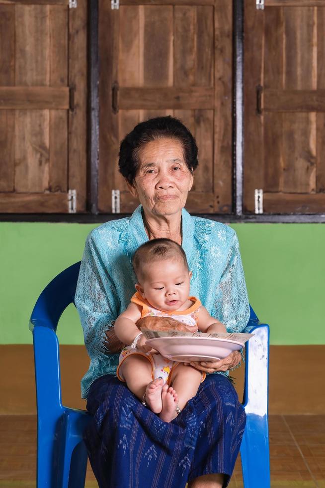 Happy senior woman holding adorable baby boy on lap smiling and looking at camera. photo