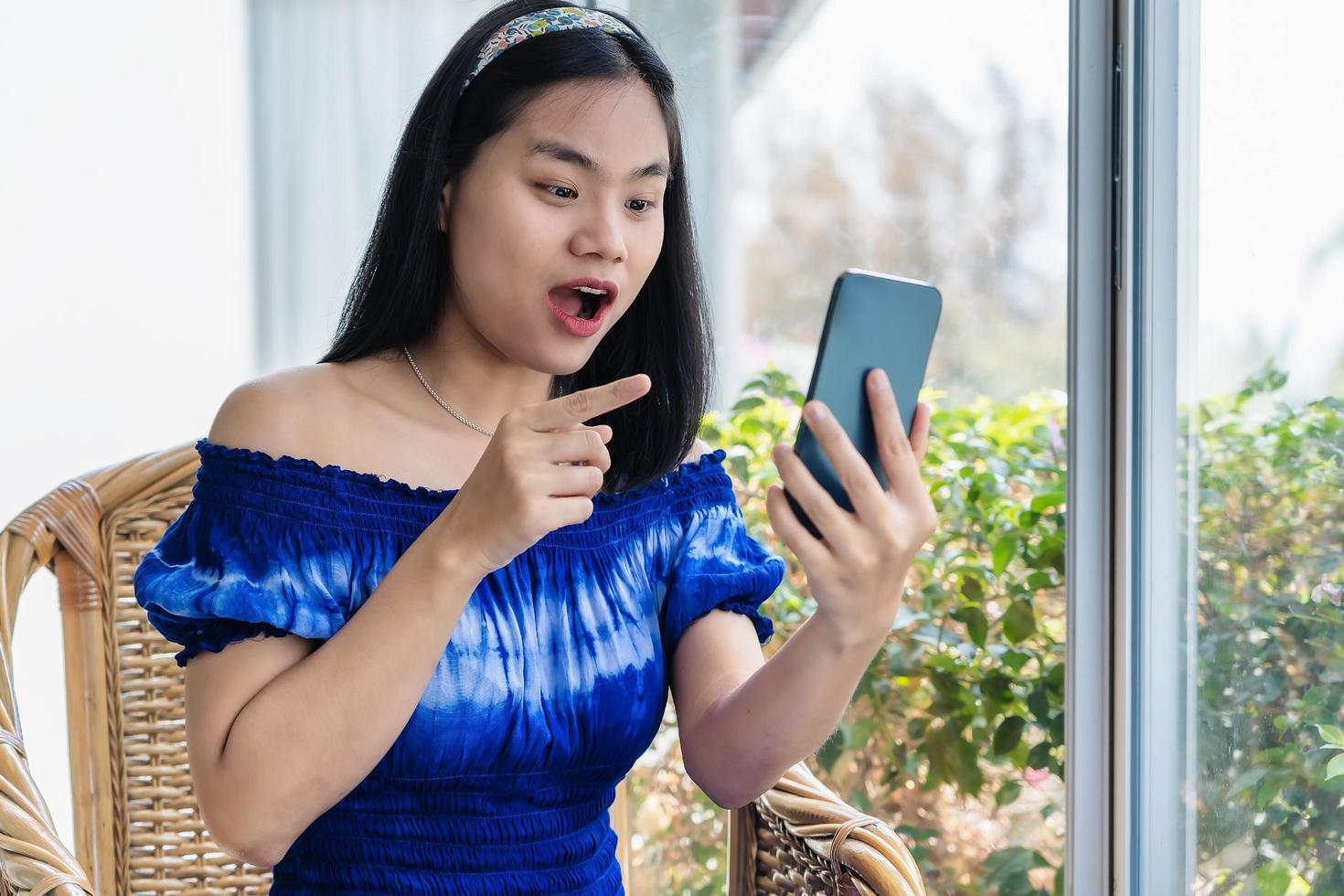 Pretty Asian young woman holding smartphone using mobile phone app for video call, laughing while watching funny video, photo