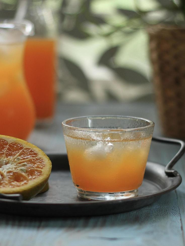 Eye angle view a glass of orange juice on vintage plate and blurred orange juice jar and window leaf pattern in the back. photo