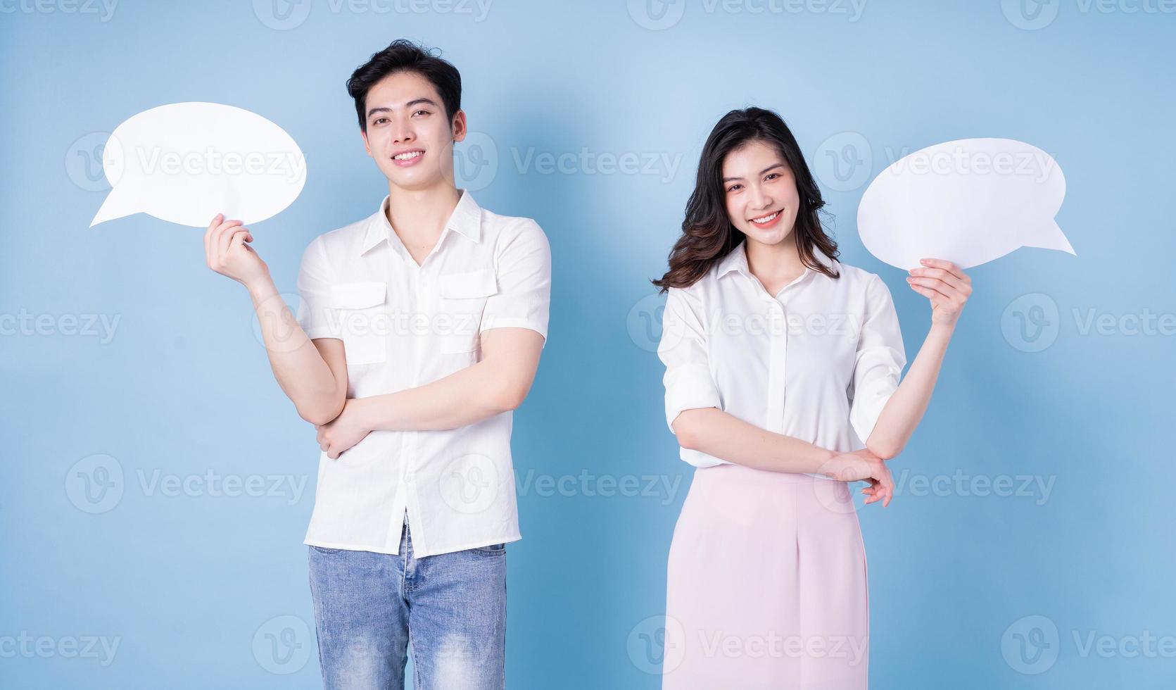 Image of young Asian couple holding message bubble on blue background photo