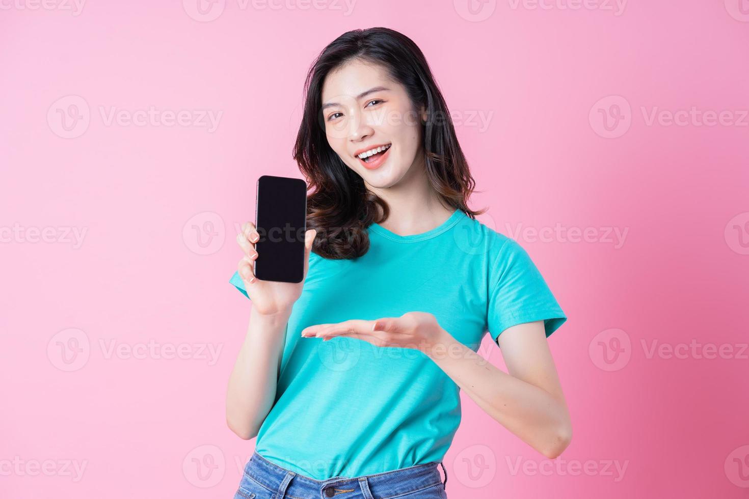 Joven mujer asiática con smartphone sobre fondo rosa foto