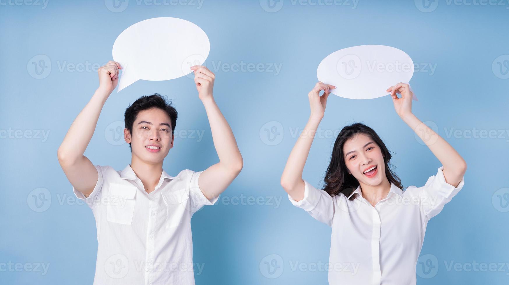 Image of young Asian couple holding message bubble on blue background photo