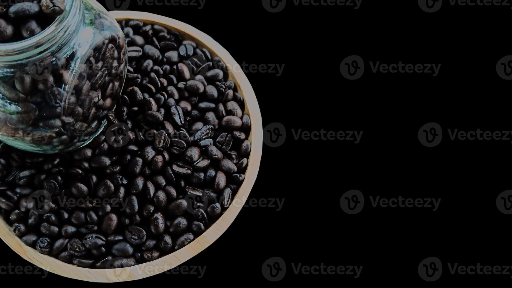 Top view, coffee beans from a glass bottle on a wooden plate on a black background photo