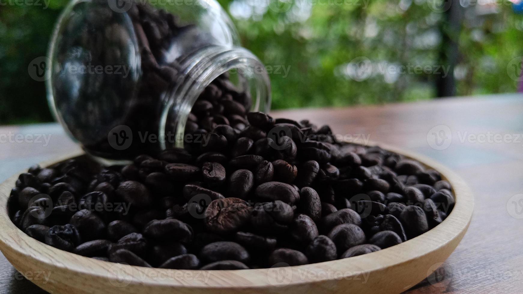 close up side view Coffee beans from a glass bottle on a wooden plate photo