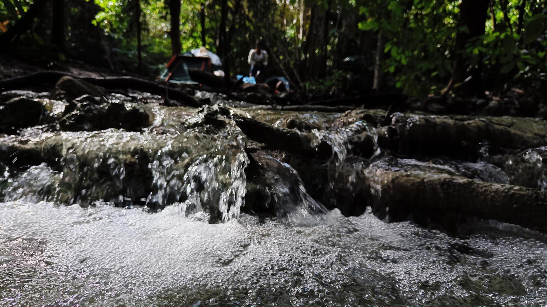 Small and narrow stream the dense green forest on early spring Blurred background. Tourists spread out tents to relax. photo