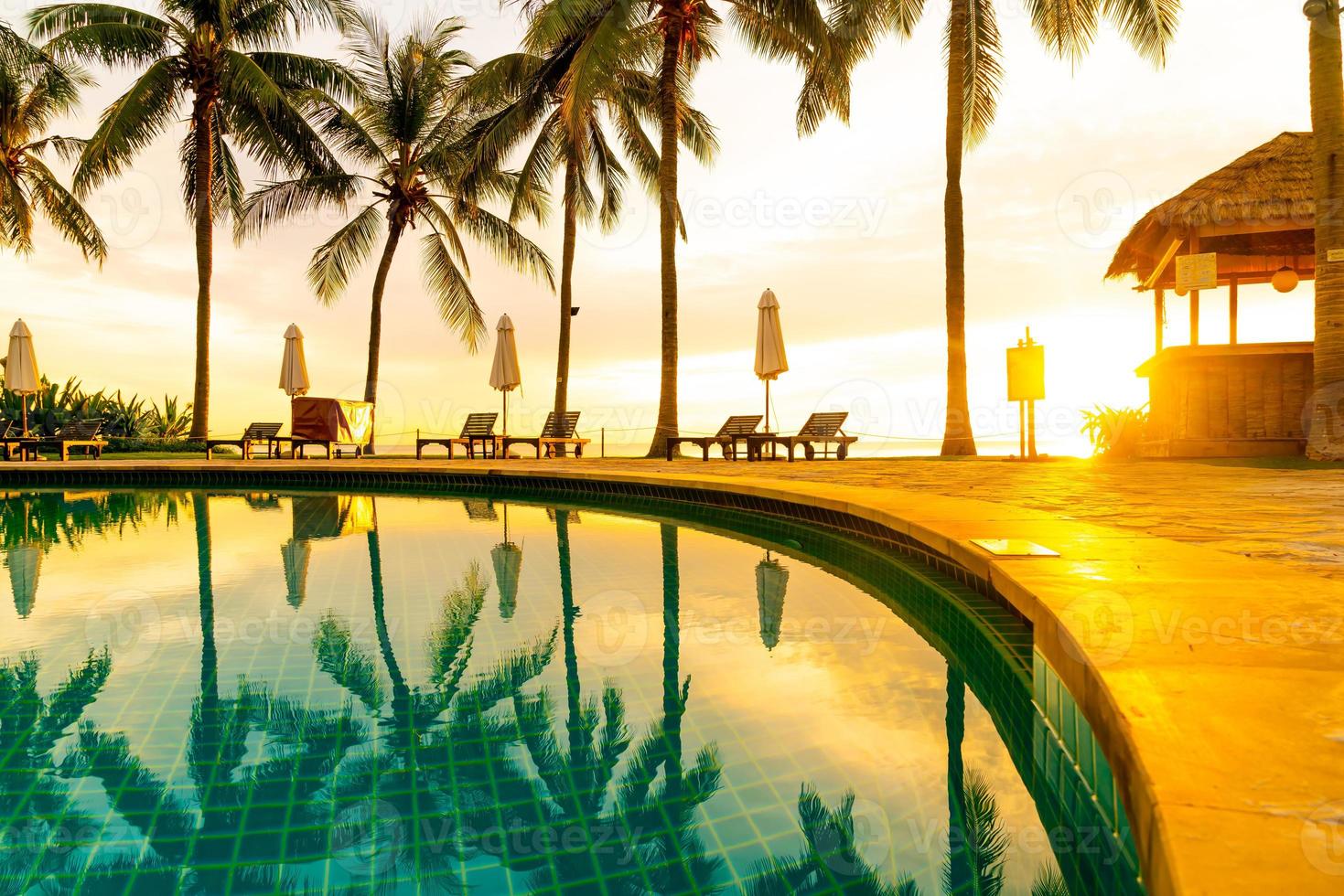 Umbrella and chair around swimming pool in hotel resort with sunrise in morning photo