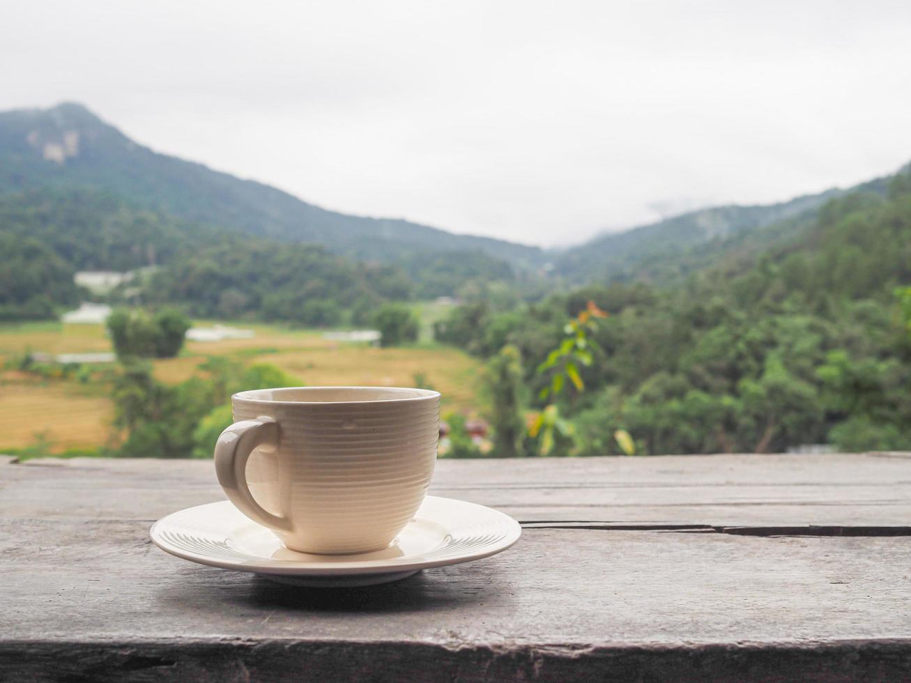 A cup of coffee on wooden table with mountains background photo