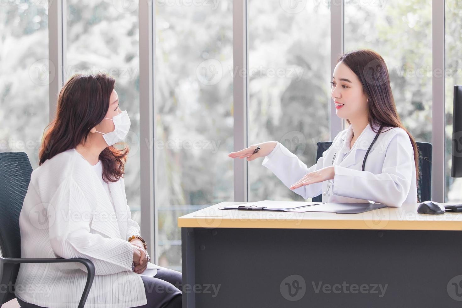 Professional Asian doctor woman who wears medical coat talks with woman patient to suggest treatment guideline and healthcare concept in office of hospital. photo