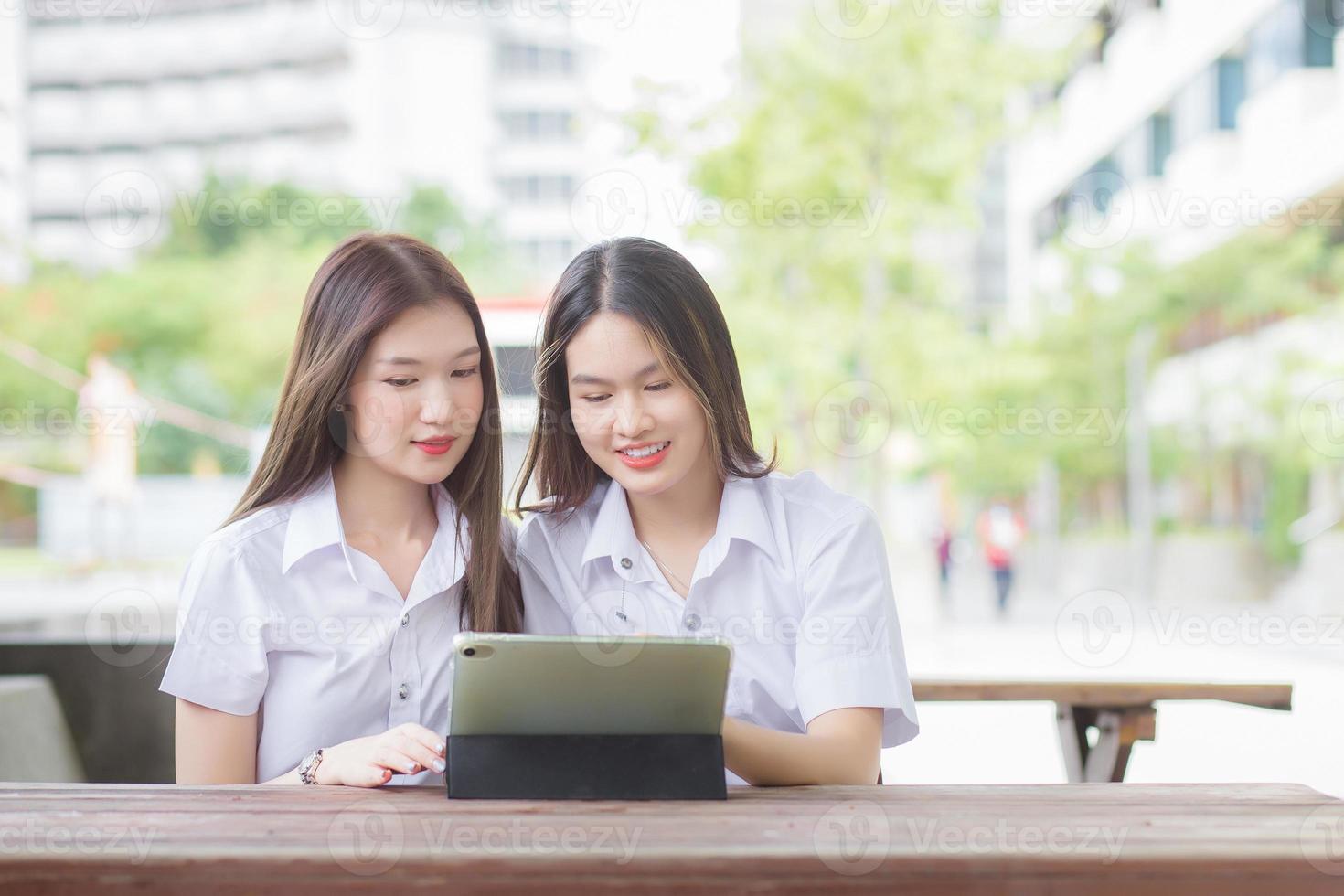 dos jóvenes estudiantes asiáticas están consultando juntas y usando una tableta para buscar información para un informe de estudio. foto