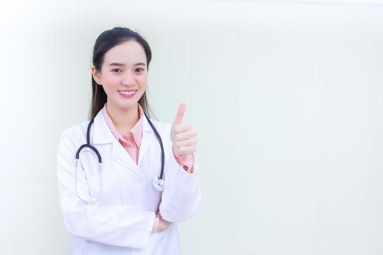 Asian woman doctor who wears medical coat shows thump up as good sign in health protection concept at hospital in health care concept photo