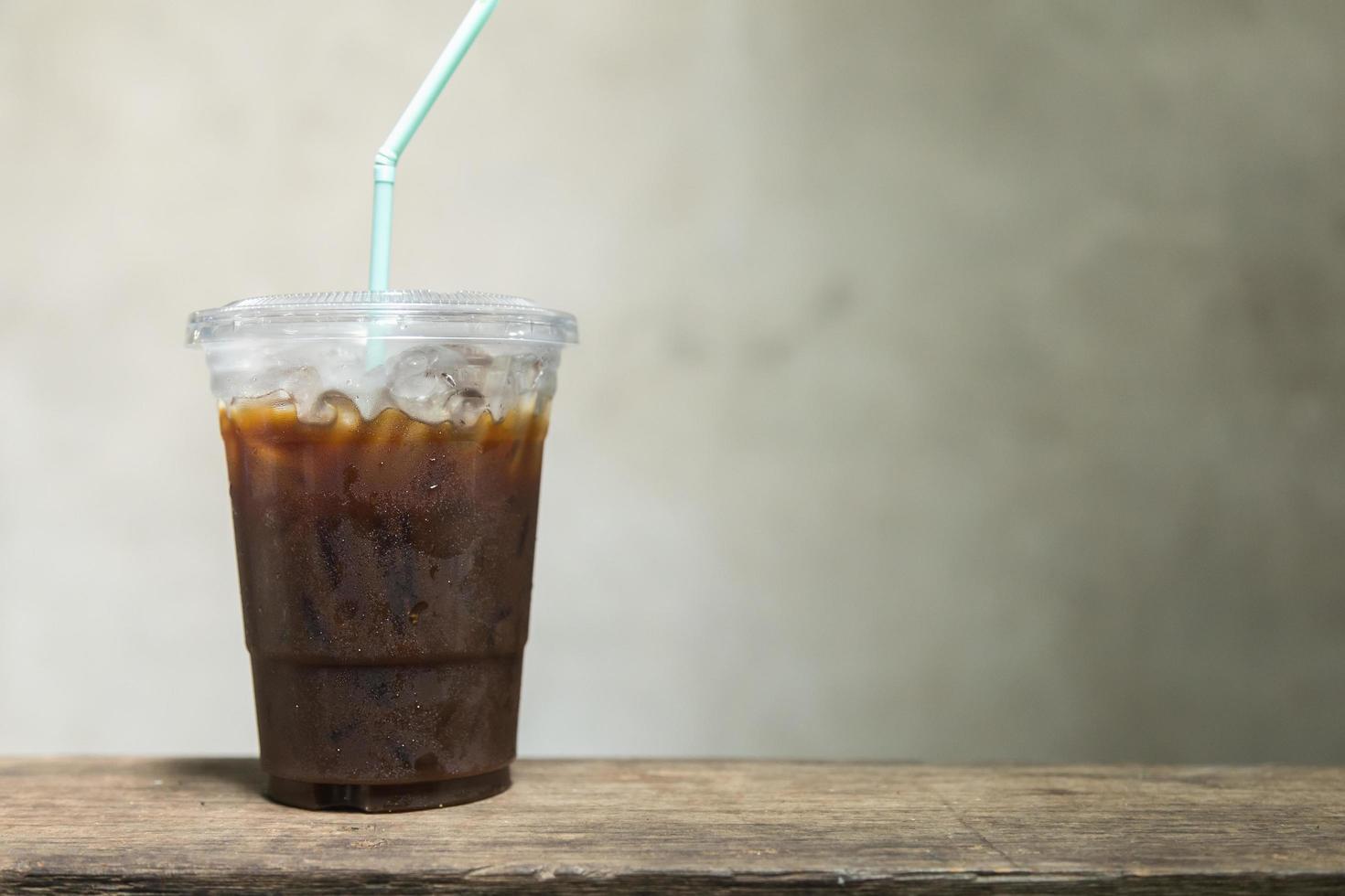 primer plano de una taza de plástico para llevar de café negro helado americano sobre una mesa de madera con espacio para copiar. foto