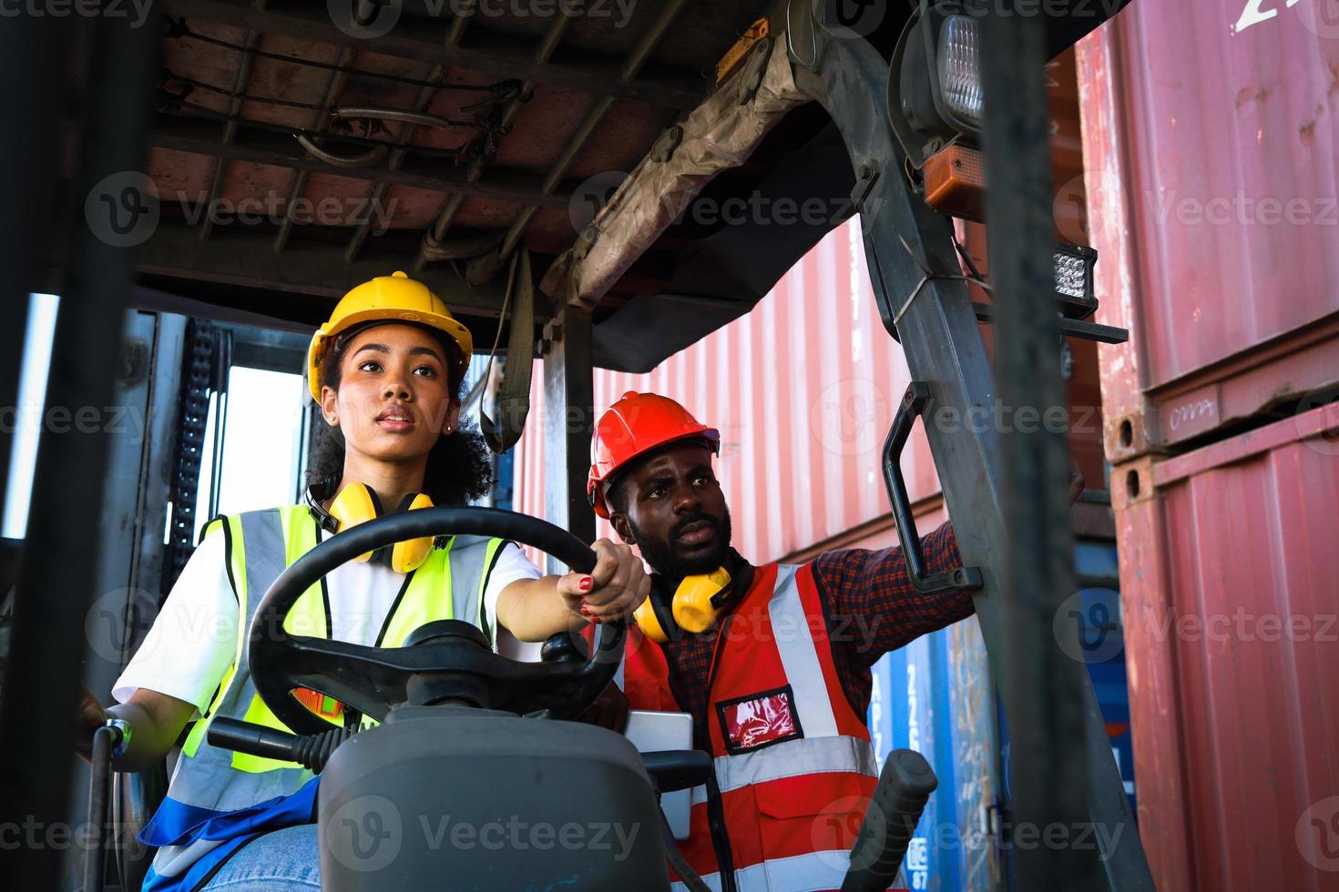 los trabajadores industriales usan chalecos de seguridad y cascos para conducir un camión montacargas en la industria de la fábrica, dos ingenieros afroamericanos, un hombre y una mujer, trabajan juntos en el patio de contenedores de carga de envío logístico. foto