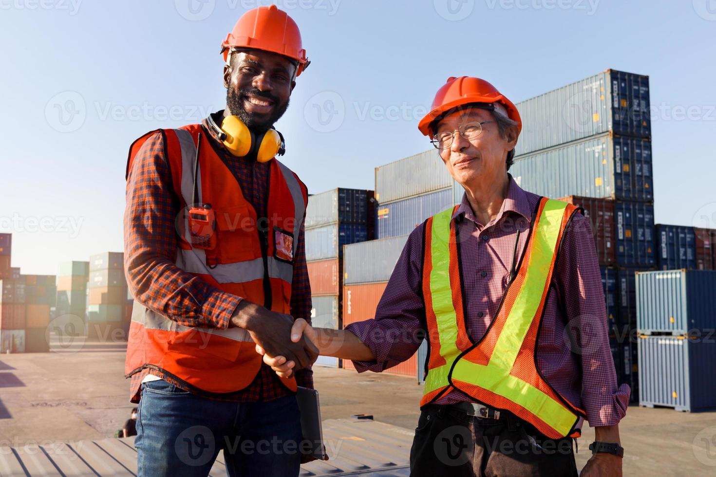 trabajador con casco de seguridad dándose la mano en el patio de contenedores de carga de envío logístico. ingeniero afroamericano hombre que tiene una choza de mano con un ingeniero trabajador asiático mayor después de una discusión de trabajo foto