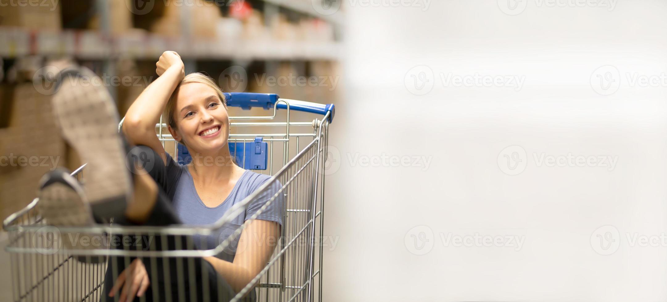 una alegre clienta con una sonrisa y mirando hacia arriba mientras se sienta en un carrito de compras en una ferretería foto