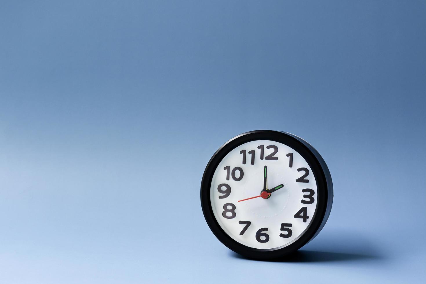 Black alarm clock isolated on blue background. The clock set at 2 o'clock. photo