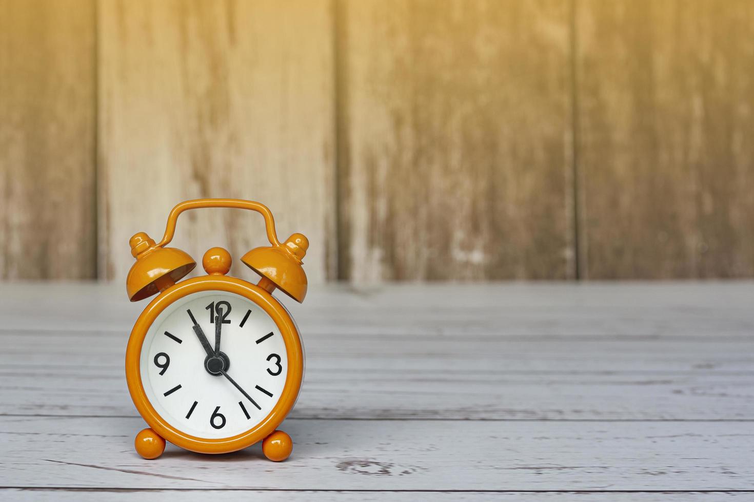 Orange alarm clock isolated on wooden desk. The clock set at 11 o'clock. photo