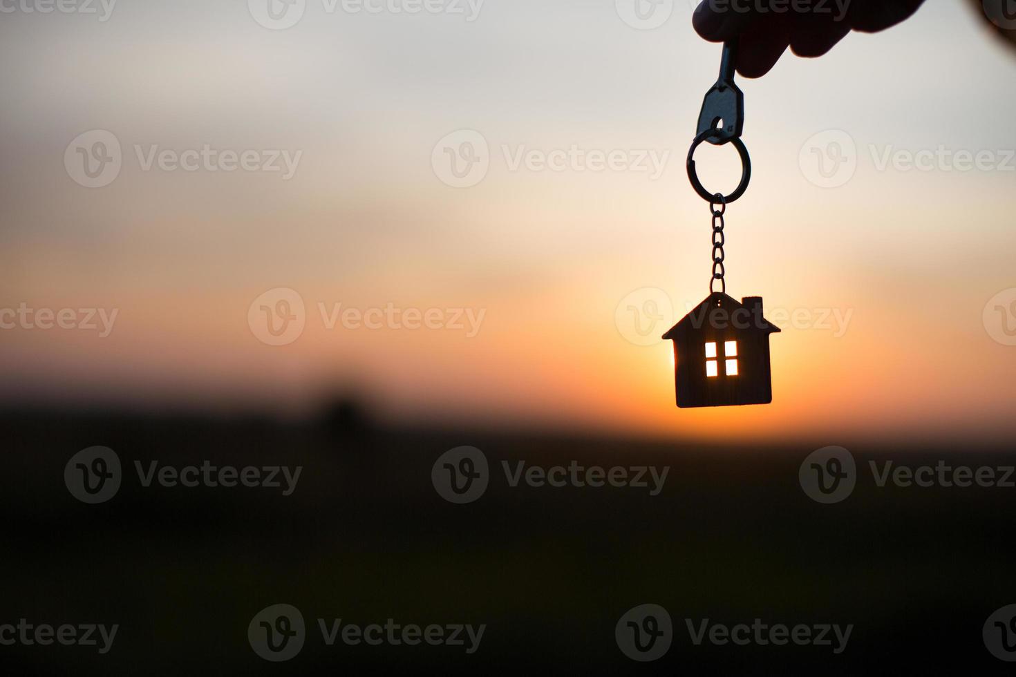 silueta de una figura de casa con una llave, un bolígrafo con un llavero en el fondo de la puesta de sol. sueñan con una casa, construir, mudarse a una nueva casa, hipotecas, alquilar y comprar bienes raíces foto