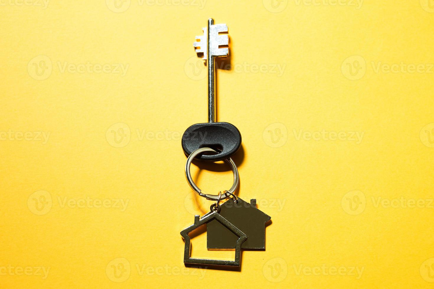 Key chain in the shape of wooden house with key on a yellow background. Building, design, project, moving to new home, mortgage, rent and purchase real estate. Copy space photo