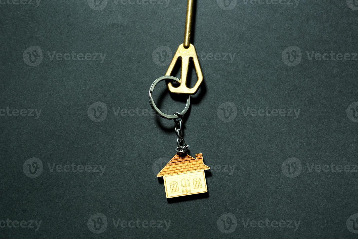 Key chain in the shape of house with key on a black background. Building, design, project, moving to new home, mortgage, deposit, rent and purchase real estate. Copy space photo