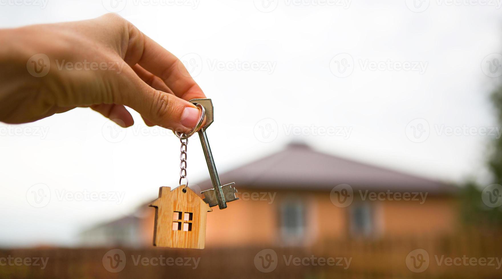 mano con una llave y una casa de llavero de madera. fondo de cerca y casa de campo. construcción, proyecto, mudanza a un nuevo hogar, hipoteca, alquiler y compra de bienes inmuebles. para abrir la puerta. copie el espacio foto