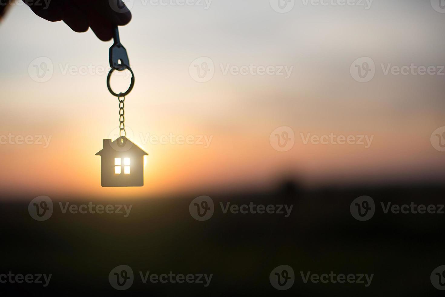 Silhouette of a house figure with a key, a pen with a keychain on the background of the sunset. They dream of a house, building, moving to a new house, mortgages, renting and buying real estate. photo
