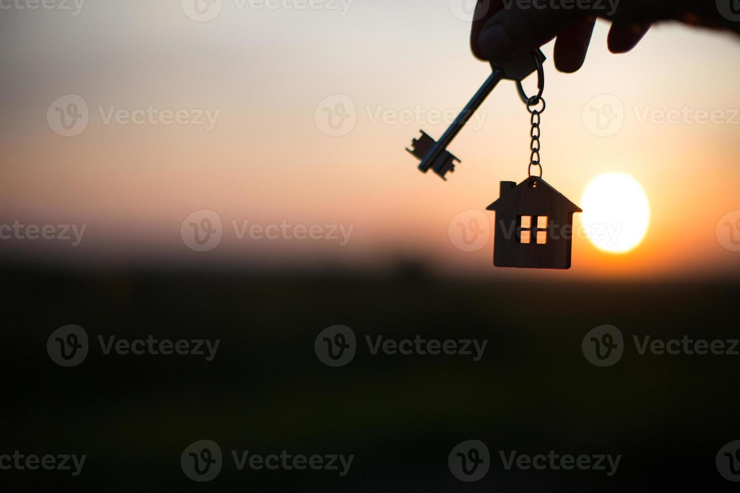 silueta de una figura de casa con una llave, un bolígrafo con un llavero en el fondo de la puesta de sol. sueñan con una casa, construir, mudarse a una nueva casa, hipotecas, alquilar y comprar bienes raíces foto