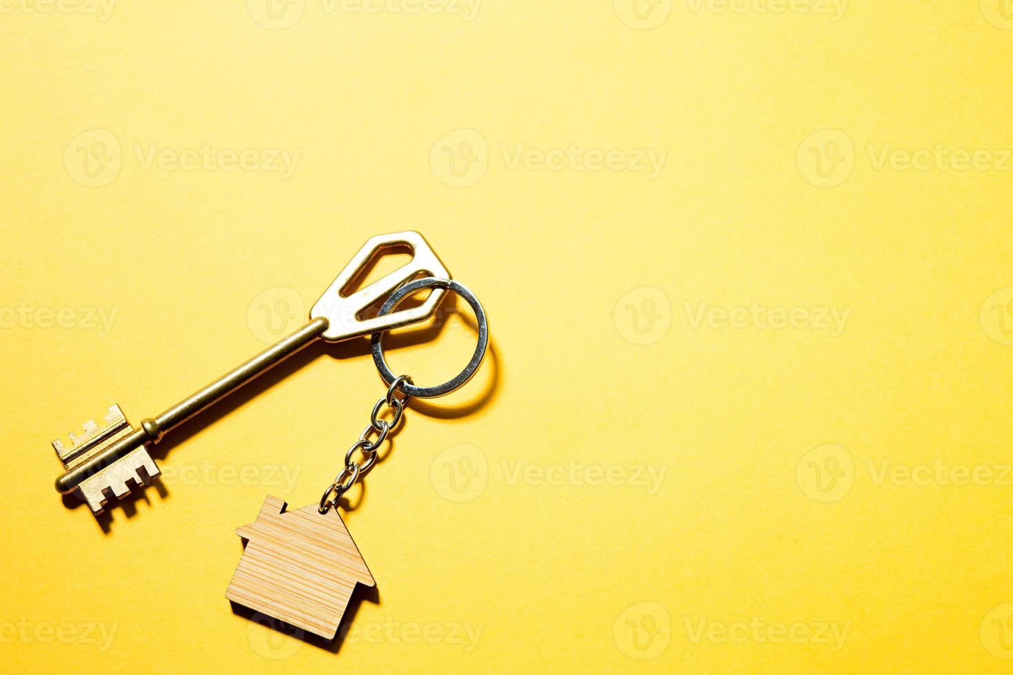 Key chain in the shape of wooden house with key on a yellow background. Building, design, project, moving to new home, mortgage, rent and purchase real estate. Copy space photo