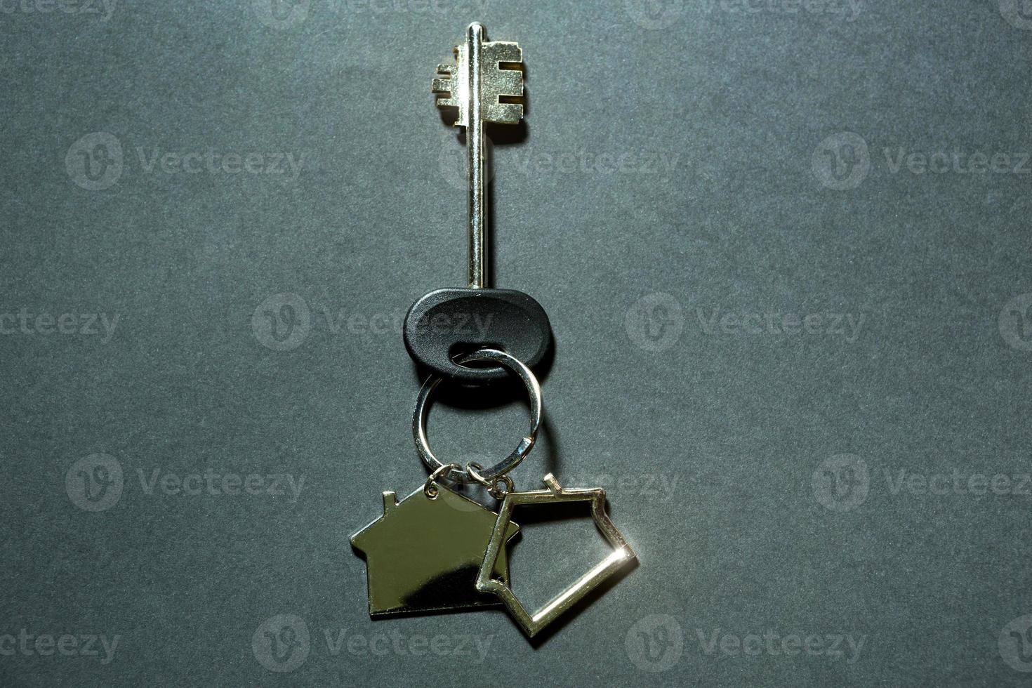 Key chain in the shape of house with key on a black background. Building, design, project, moving to new home, mortgage, deposit, rent and purchase real estate. Copy space photo