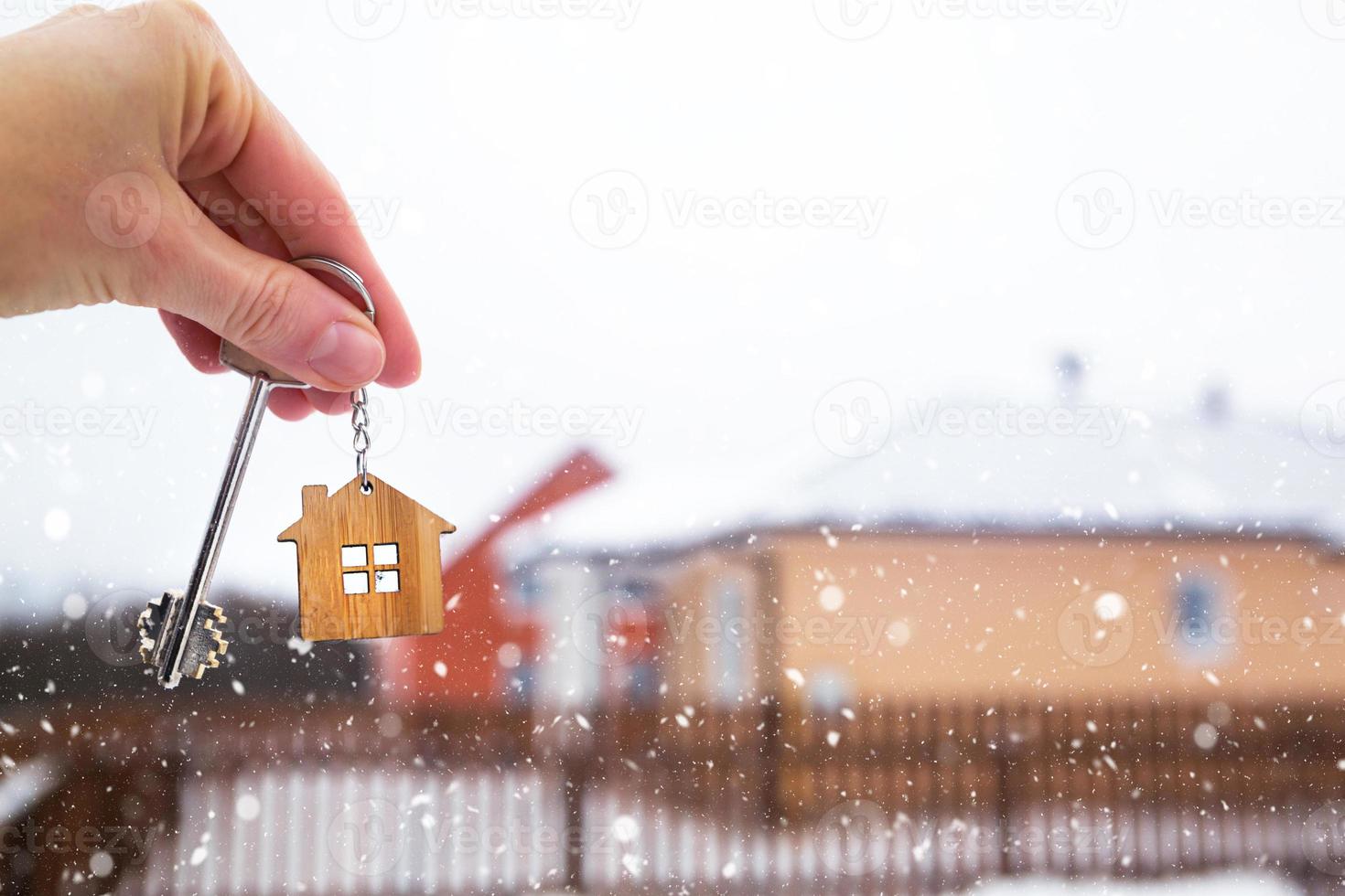 Hand with a Key of the house in winter in the snow. Background of fence and cottage. Give a gift for New Year, Christmas. Moving to new house, mortgage, rent and purchase real estate. Open the door. photo
