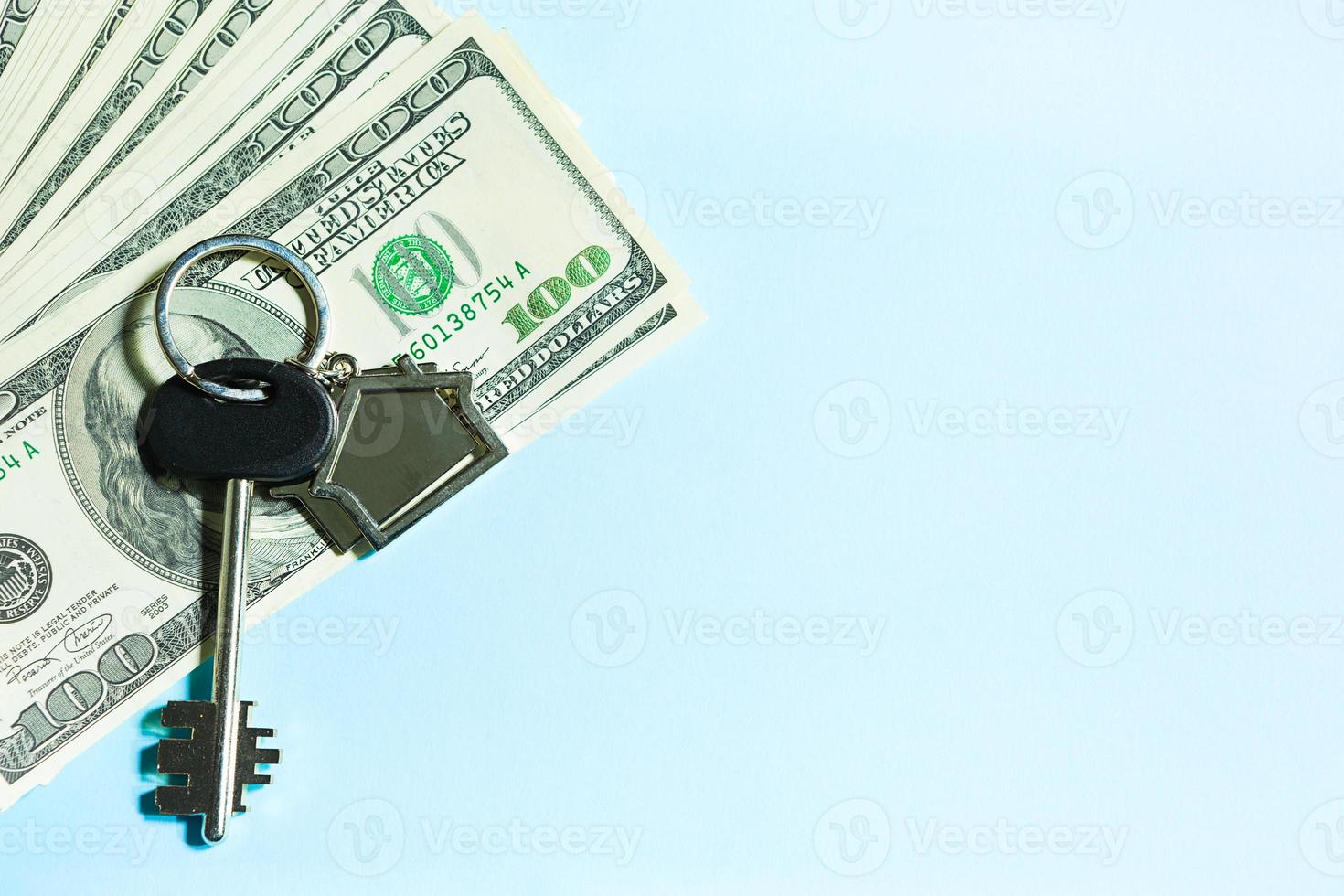 Home key with a keychain on a stack of  100 bills on a blue background. Purchase of an apartment, house, real estate, business, mortgage and housing loan from bank, savings, cash, moving. Copy space photo