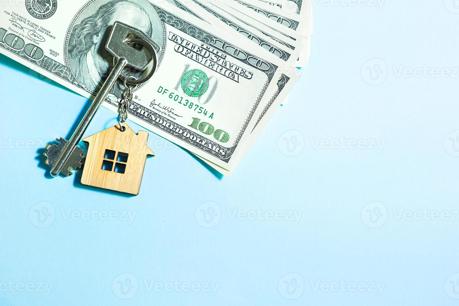 Home key with a keychain on a stack of  100 bills on a blue background. Purchase of an apartment, house, real estate, business, mortgage and housing loan from bank, savings, cash, moving. Copy space photo