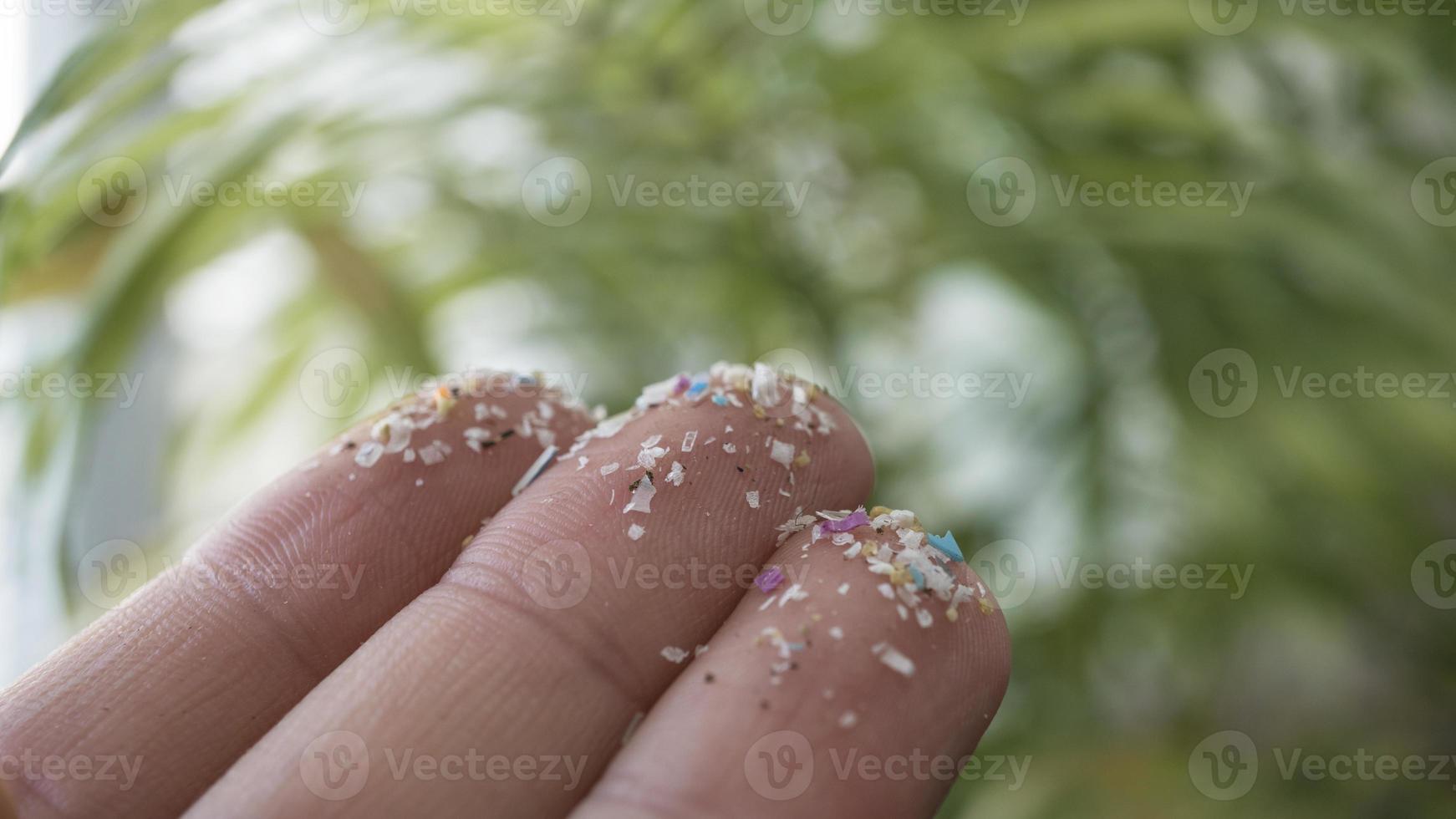 primer plano lateral de microplásticos en los dedos humanos. concepto de contaminación del agua y calentamiento global. idea del cambio climático. enfoque suave en un montón de microplásticos que no se pueden reciclar. foto