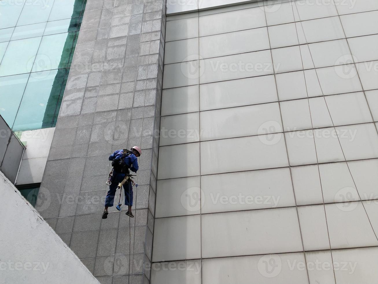 photo of a worker cleaning the outside of the building, hanging from a safety rope