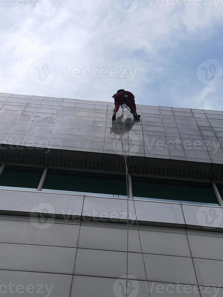 photo of a worker cleaning the outside of the building, hanging from a safety rope