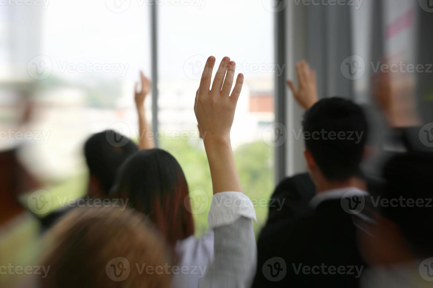vista trasera de gente de negocios en seminario levantando la mano para votar en la actividad de la reunión o evento de negocios haciendo preguntas en el seminario o taller del orador foto