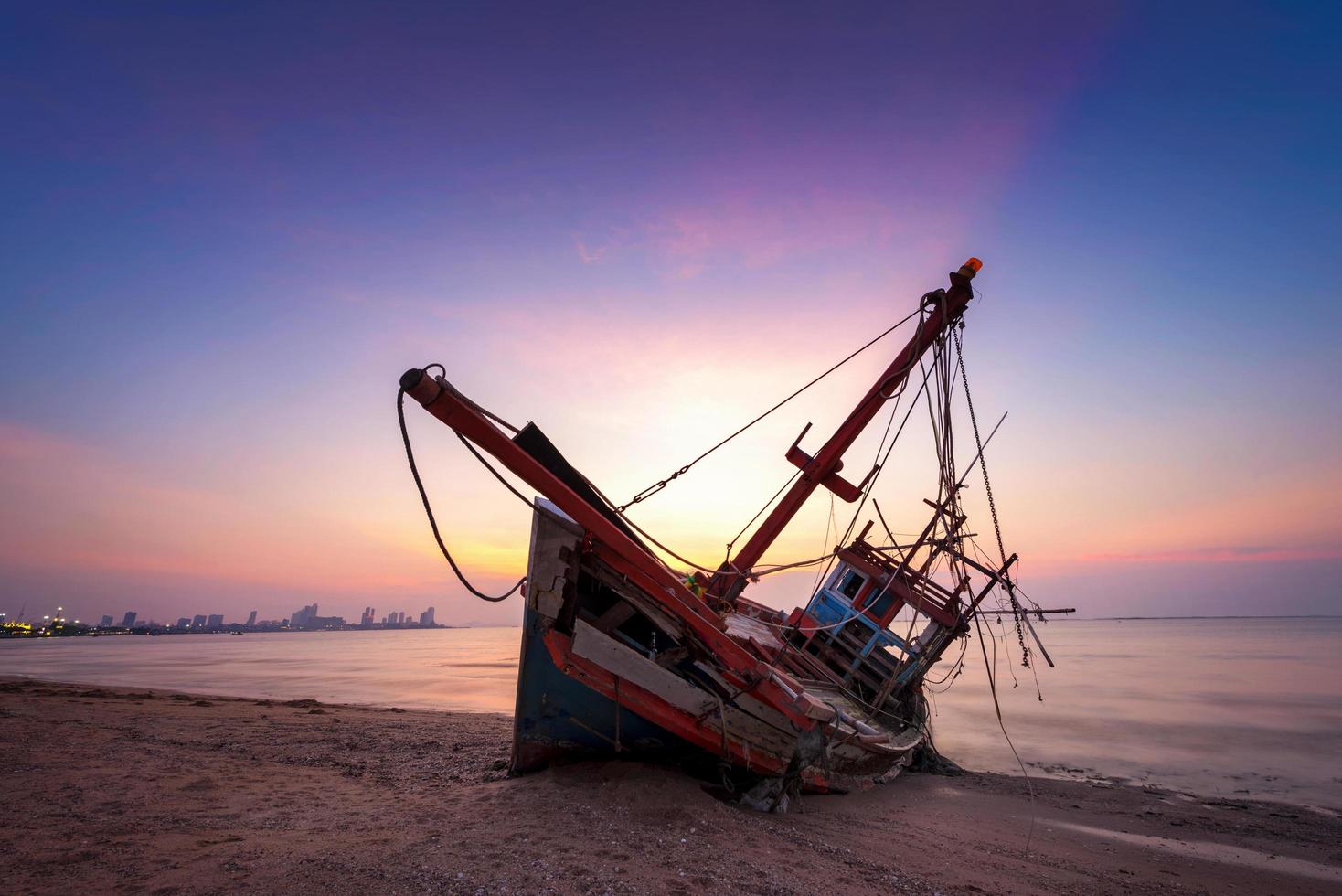 naufragio abandonado de un barco de pesca de madera en la playa a la hora del crepúsculo foto