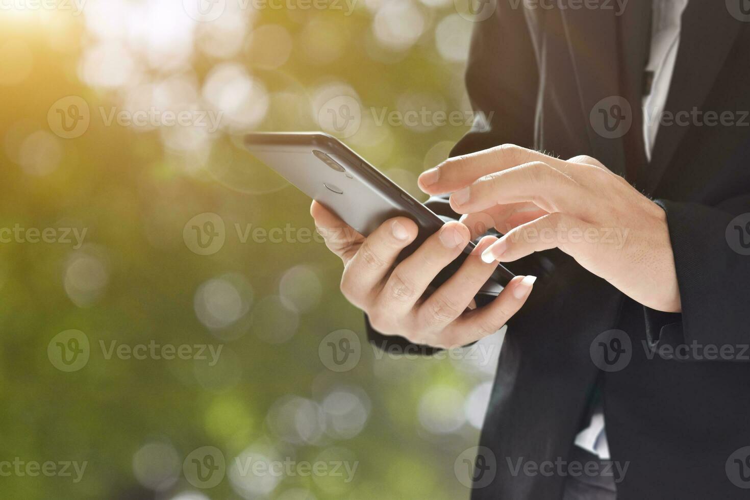 Closeup image of man holding and using mobile phone on bokeh background outdoor. photo