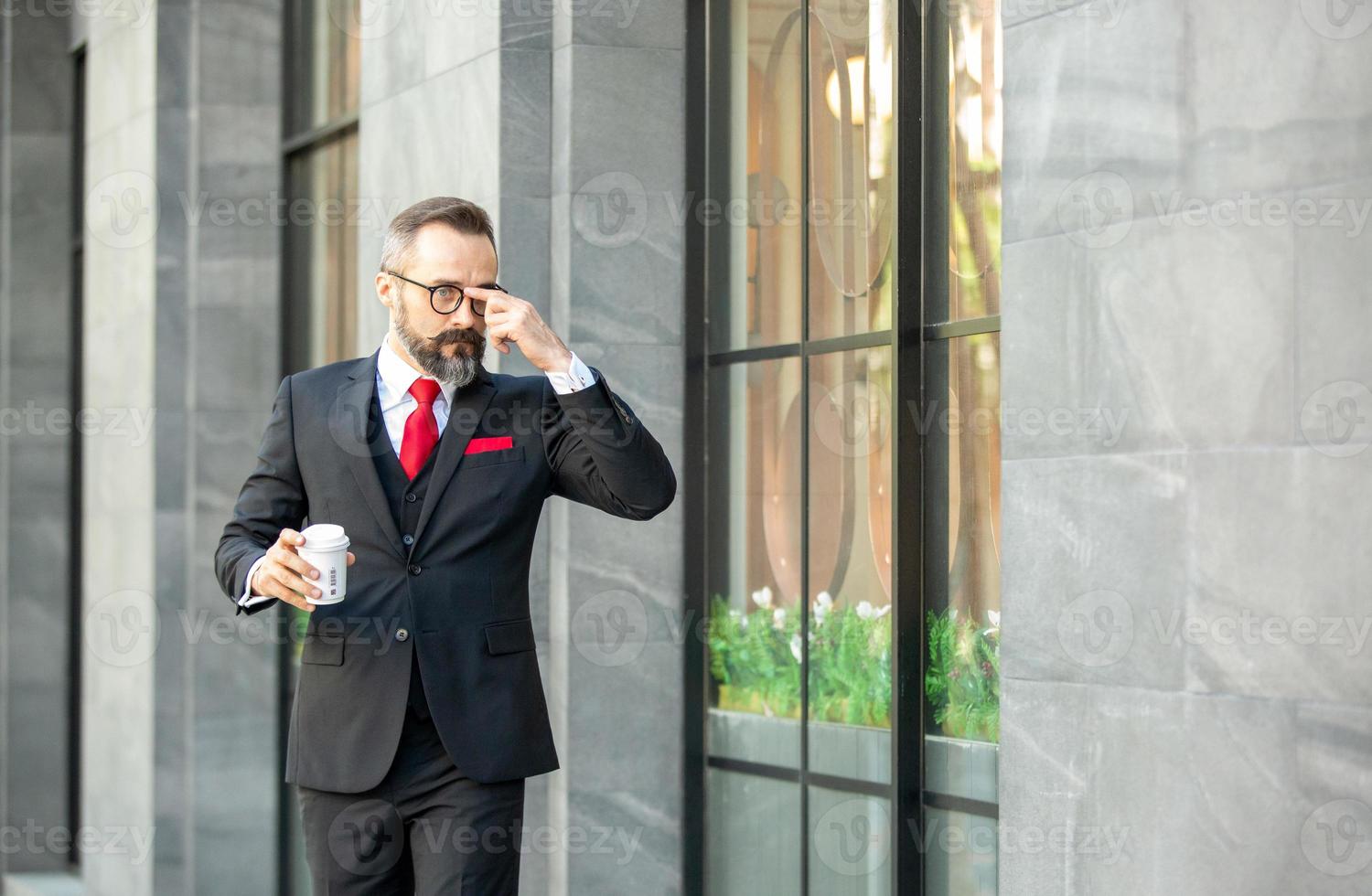 hombre de negocios hipster en traje de pie con una taza de café cerca de la oficina al aire libre foto