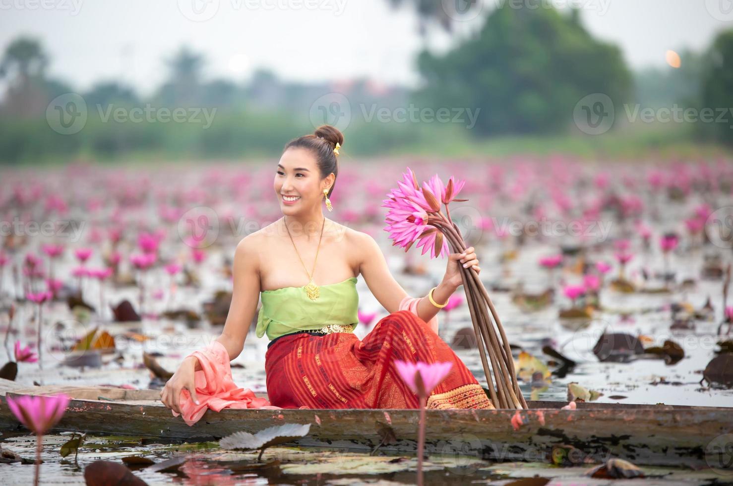 Young Asian women in Traditional dress in the boat and pink lotus flowers in the pond.Beautiful girls in traditional costume.Thai girl in retro Thai dress, Thai girl in traditional dress costume photo