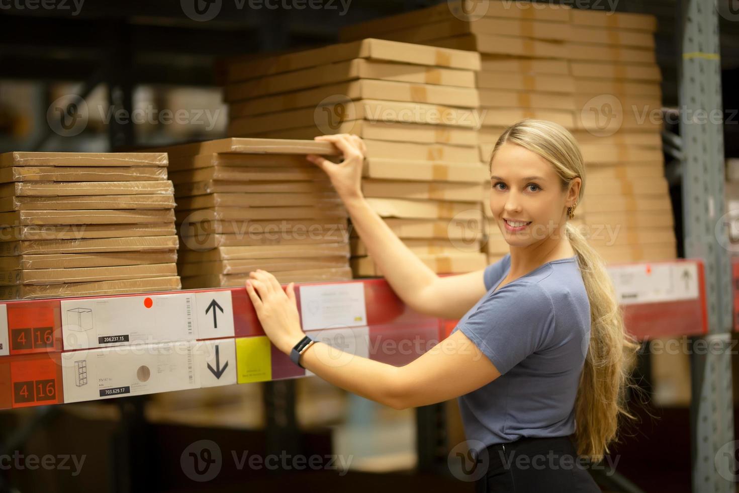 alegre mujer cliente mirando hacia arriba y tirando del producto en el estante mientras compra en la ferretería foto