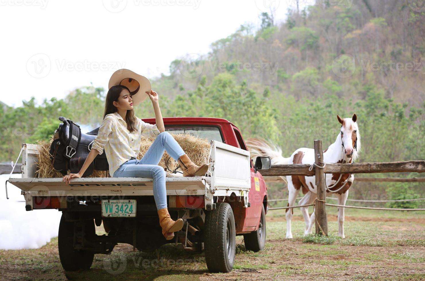 Cowgirl model posing on farm. A portrait of a beautiful young cowgirl leaning against a wall in a stable at farm. photo