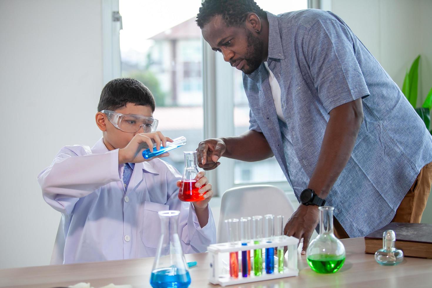 niño pequeño mezcla productos químicos en vasos de precipitados. un profesor entusiasta explica la química a los niños, un estudiante de química muestra un nuevo experimento a la clase de ciencias del profesor foto